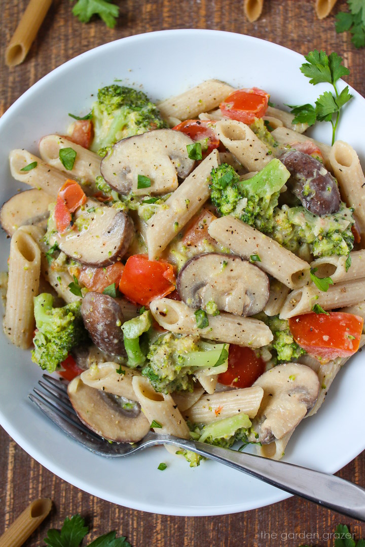 Overhead view of vegan creamy vegetable pasta served in a white bowl with fork