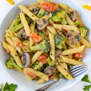 Overhead view of creamy vegetable pasta in a white bowl with serving fork