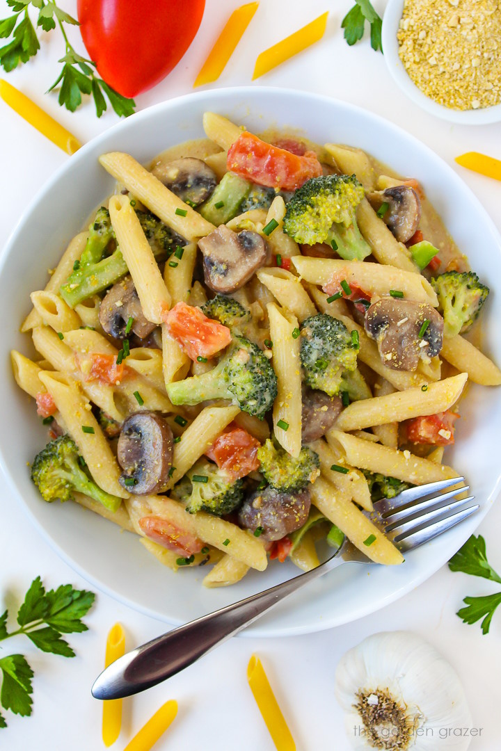 Overhead view of creamy vegetable pasta in a white bowl with serving fork