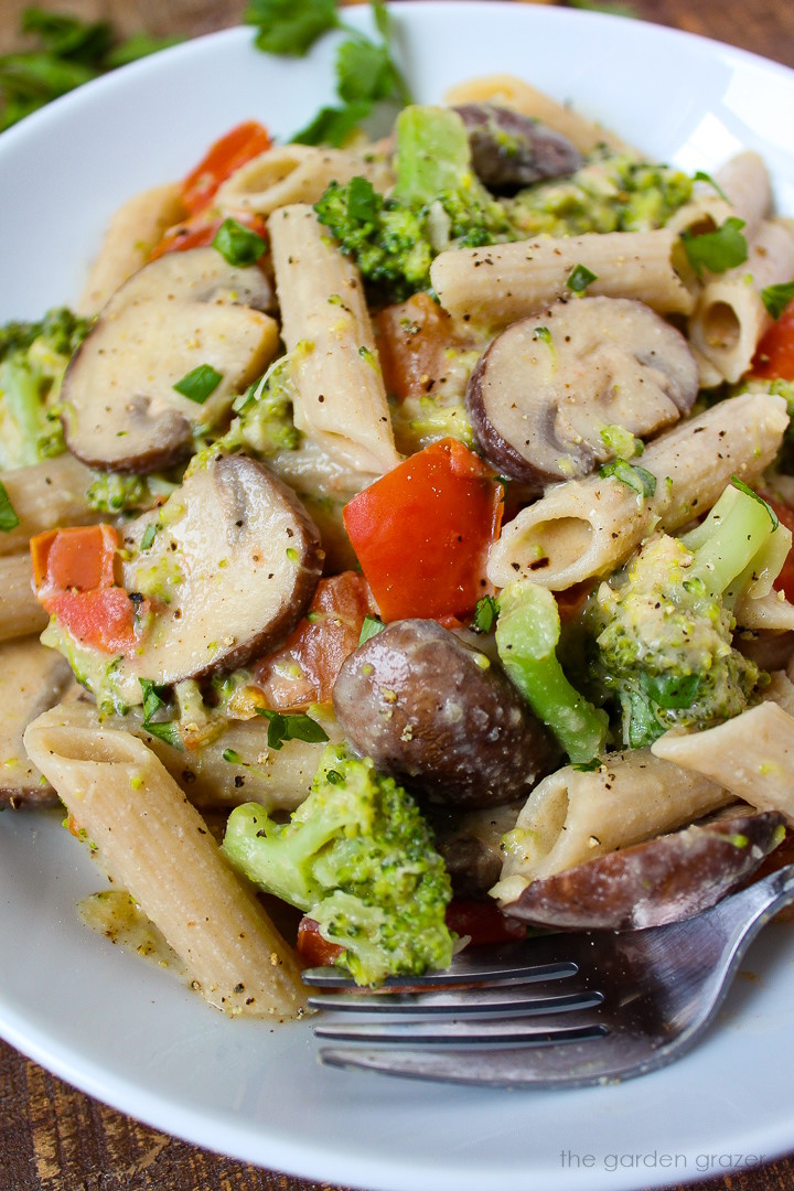 Close up view of creamy vegetable pasta in a white serving bowl with fork