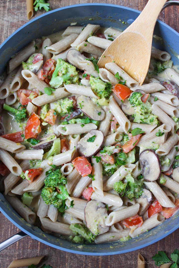 Overhead view of creamy vegetable pasta cooking in a large skillet with a stirring spoon