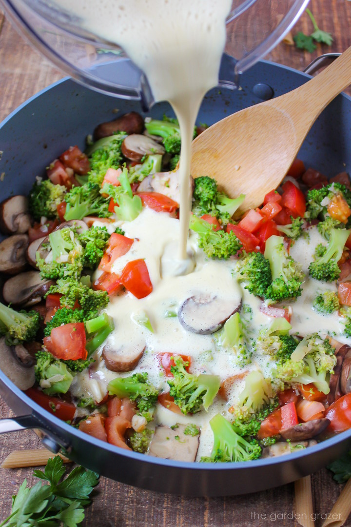 Cream sauce being poured over veggies in a cooking pan