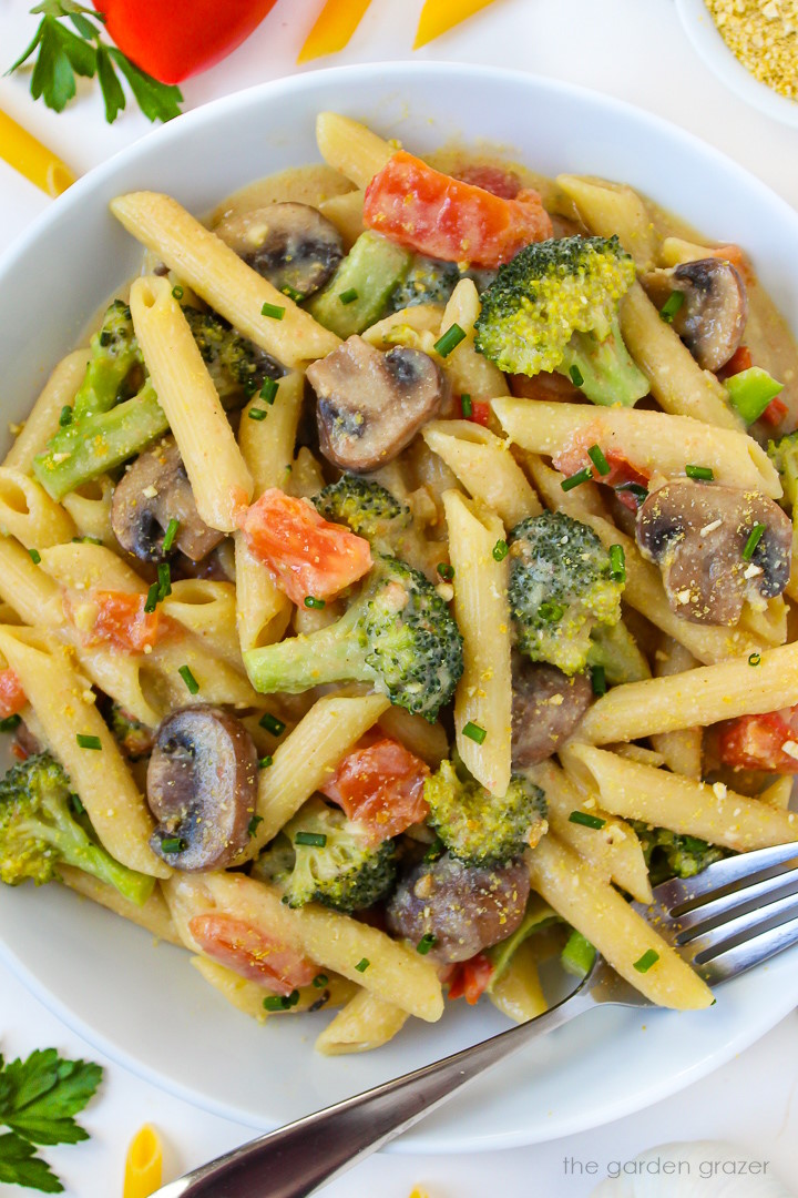 Close-up view of vegan creamy vegetable pasta in a white bowl with broccoli, mushroom, and tomato