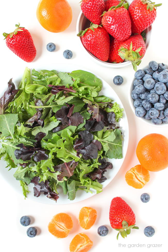 Fresh greens, strawberries, and blueberries on a white table
