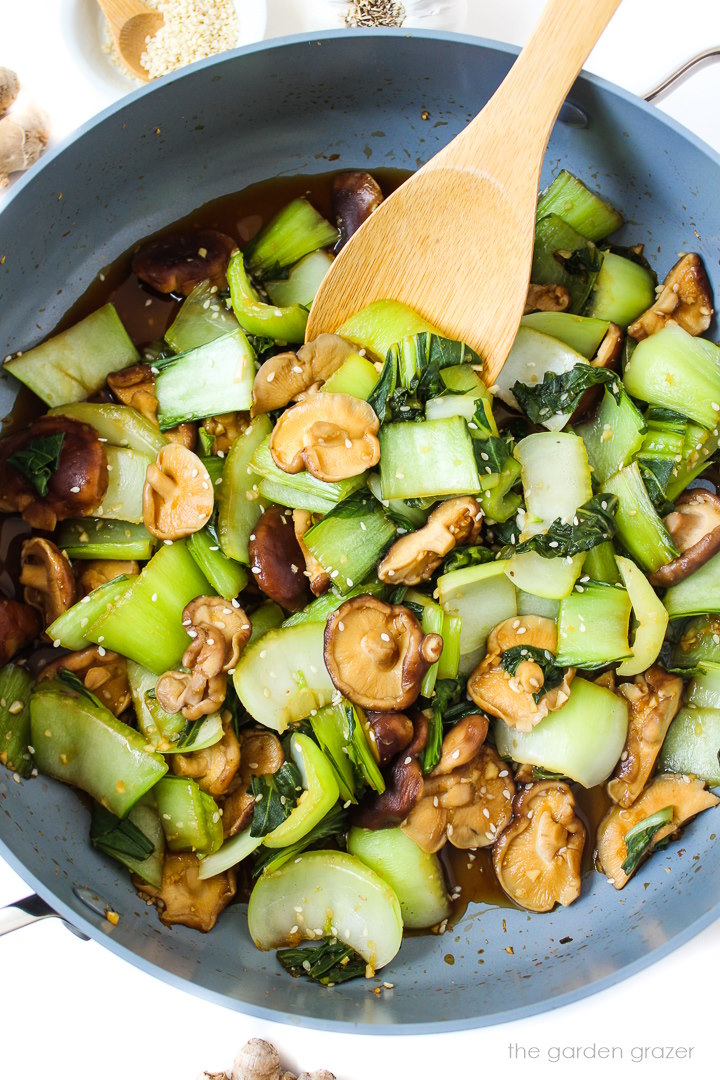 Baby bok choy and shiitake mushrooms cooking in a large skillet with garlic sauce