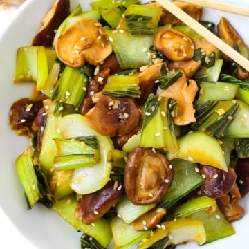 Overhead view of garlic bok choy and shiitake mushrooms on a white plate with sesame seeds