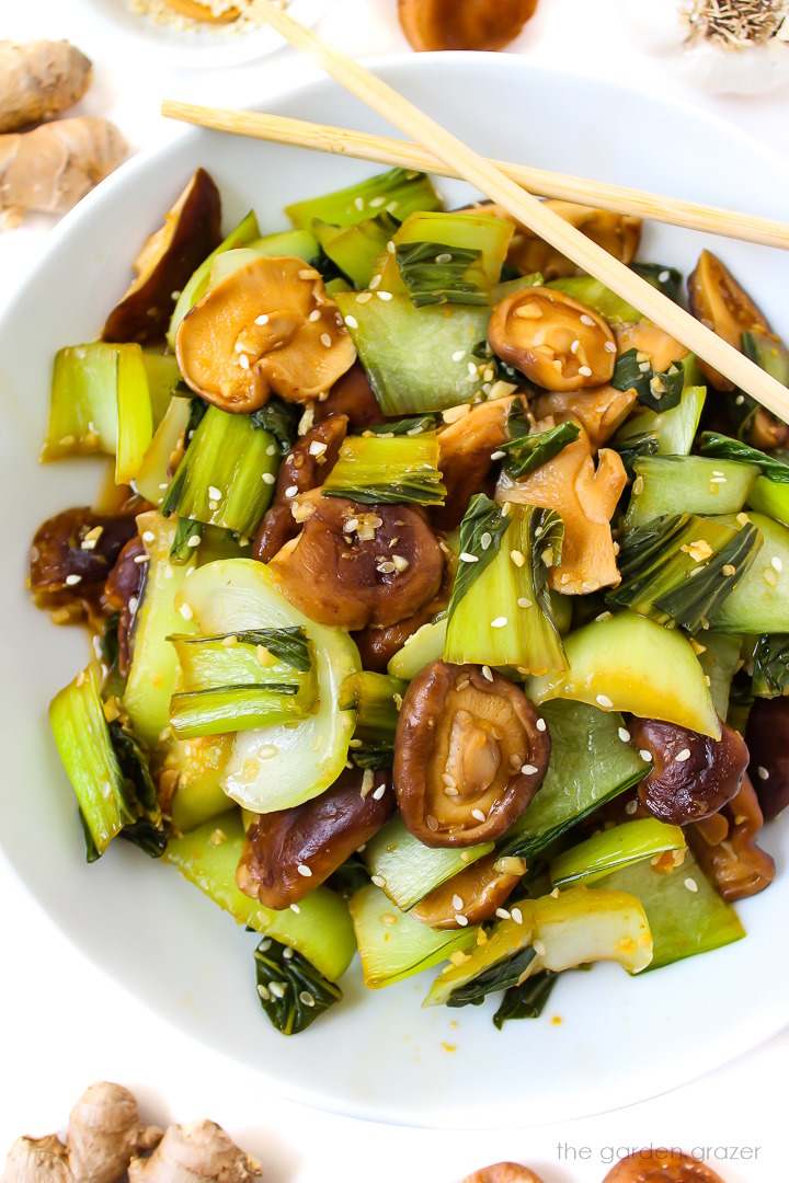 Overhead view of garlic bok choy and shiitake mushrooms on a white plate with sesame seeds