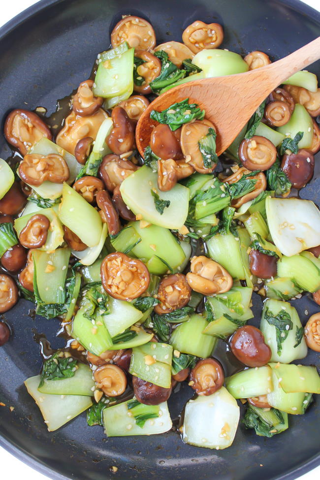 Baby bok choy and shiitake mushrooms cooking in a pan with garlic sauce