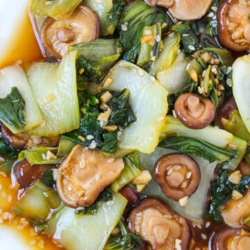 Overhead view of baby bok choy and shiitake mushrooms in a garlic sauce served on a white plate