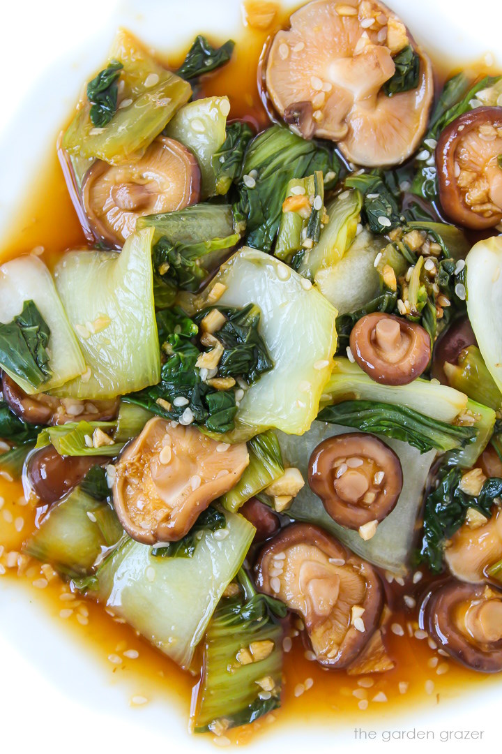 Overhead view of baby bok choy and shiitake mushrooms in a garlic sauce served on a white plate
