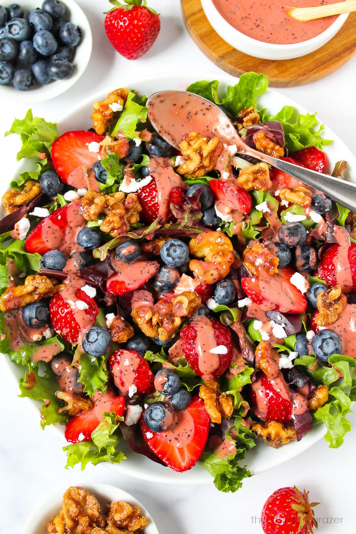 Strawberry blueberry salad in a white serving bowl topped with candied walnuts, vegan feta, and balsamic dressing