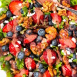 Overhead view of strawberry blueberry salad in a white serving bowl with dressing spoon