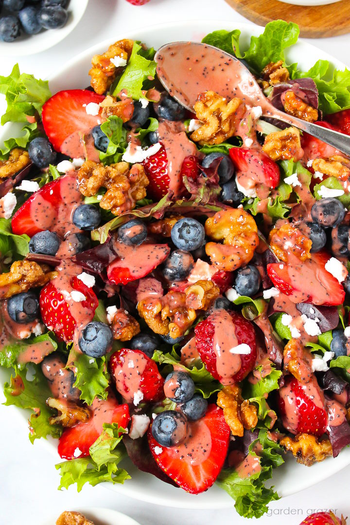 Overhead view of strawberry blueberry salad in a white serving bowl with dressing spoon