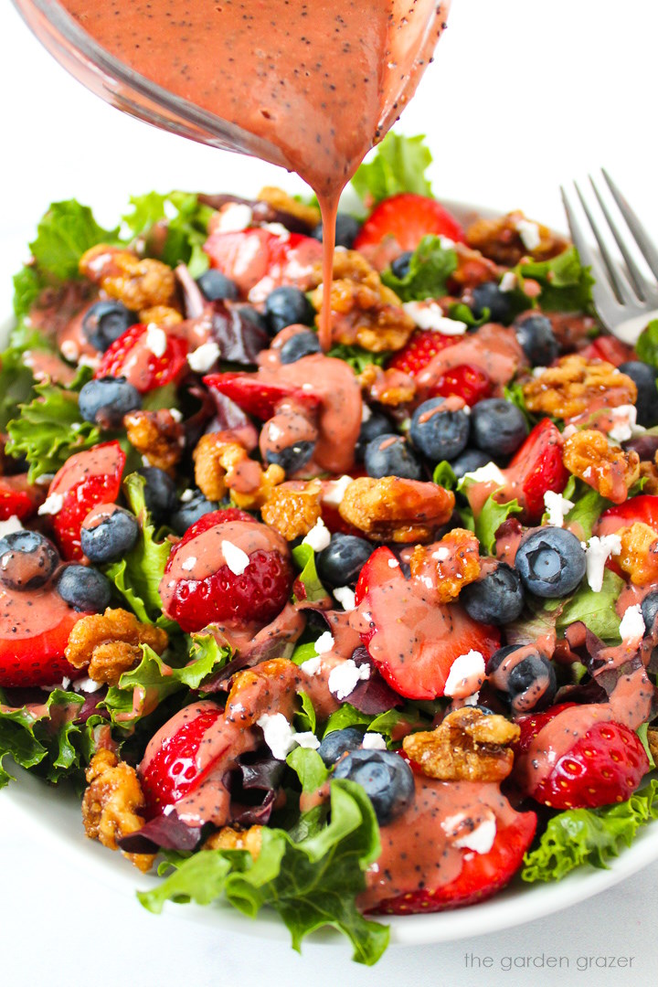 Dressing being poured over a strawberry blueberry salad in a white bowl