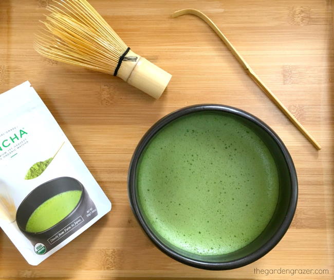 Bowl of whisked matcha sitting on bamboo tray with whisk and scoop