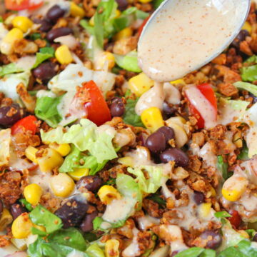 Vegan taco salad in a white bowl with dressing on a spoon