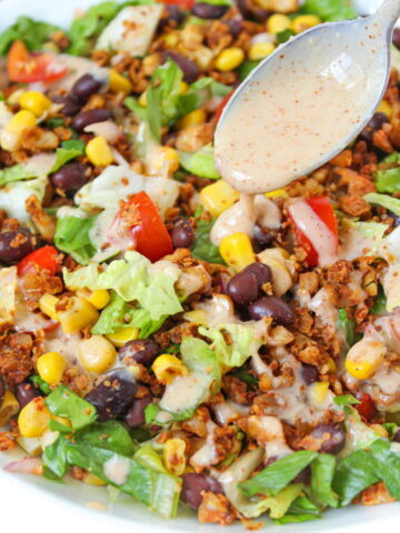 Vegan taco salad in a white bowl with dressing on a spoon