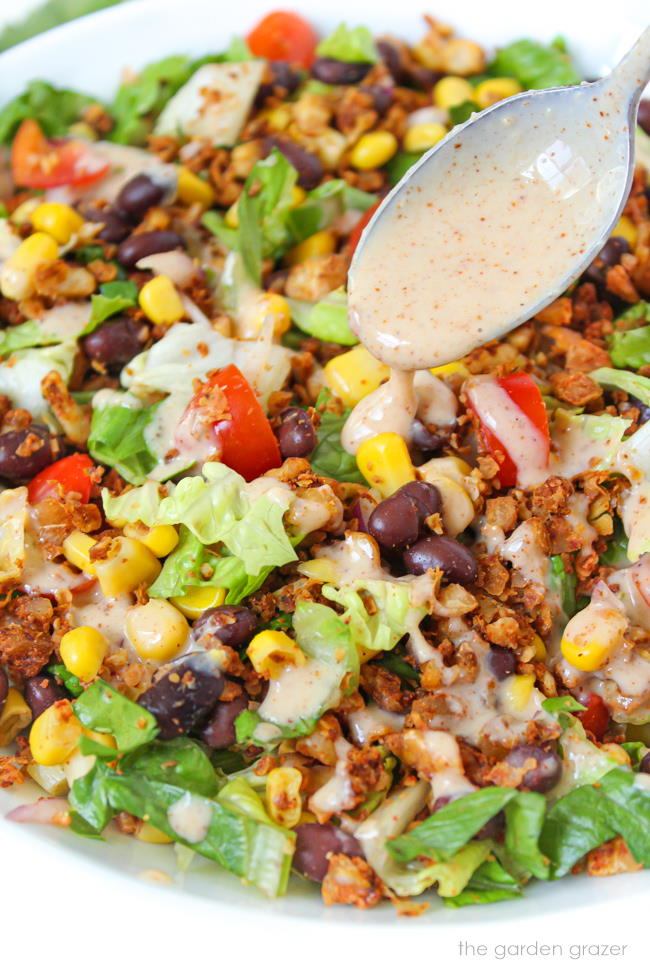 Vegan taco salad in a white bowl with dressing on a spoon