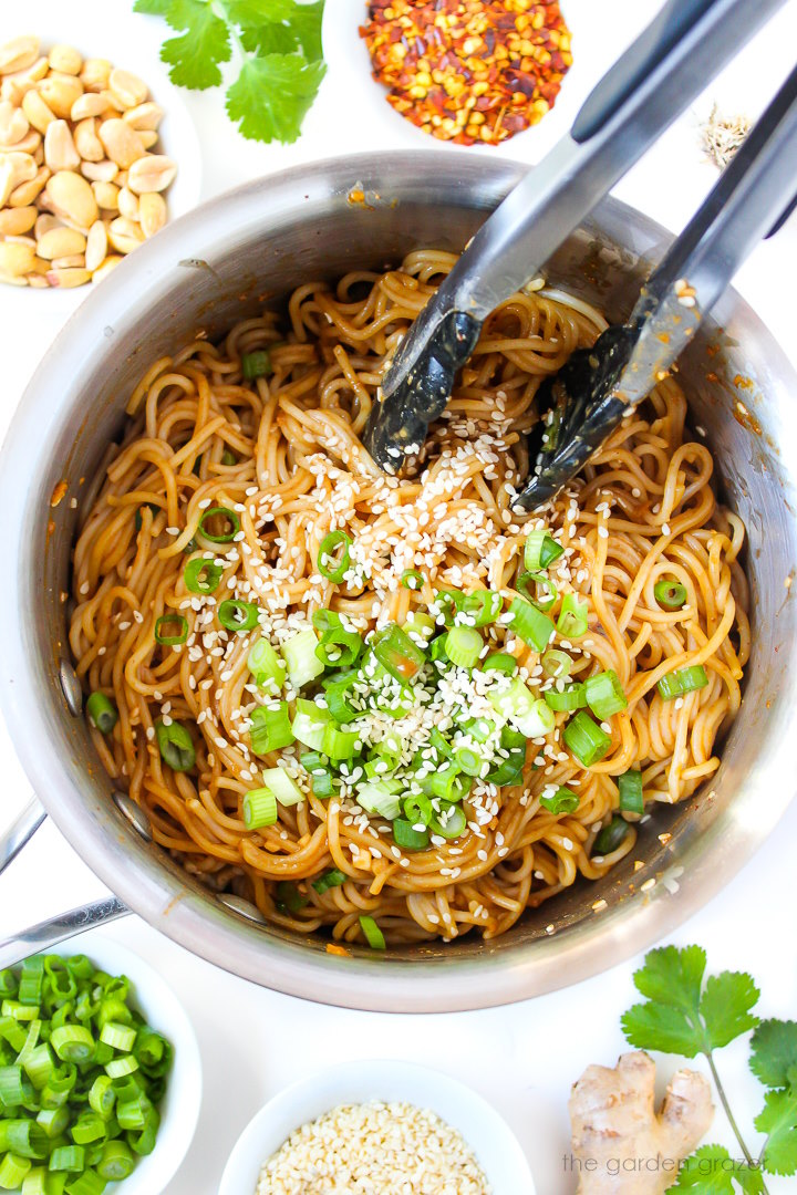 Hoisin peanut noodles cooking in a saucepan with tongs for stirring