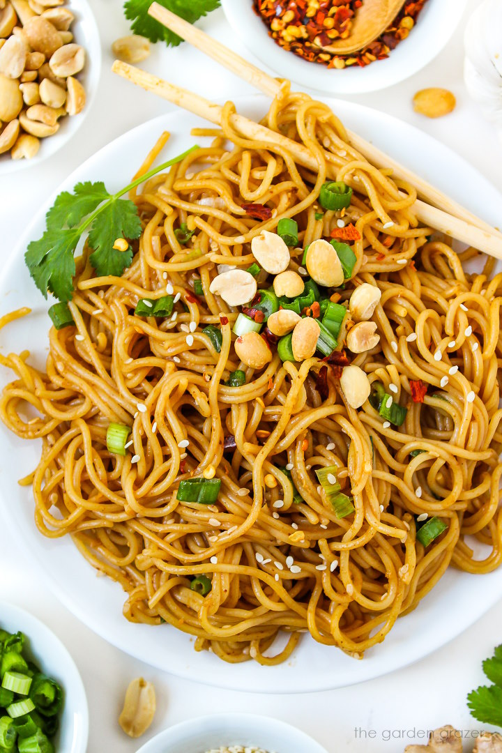 Close up view of hoisin peanut noodles on a white plate with sesame seeds and peanuts
