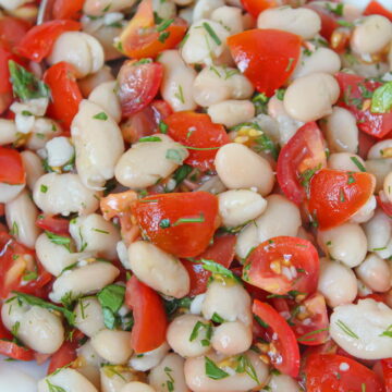 White bean salad on a white plate with fresh herbs and tomato