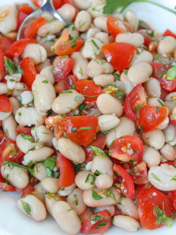 White bean salad on a white plate with fresh herbs and tomato