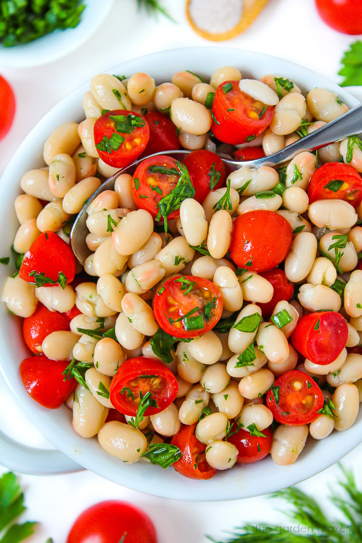 Close up view of white bean tomato salad in a bowl with serving spoon