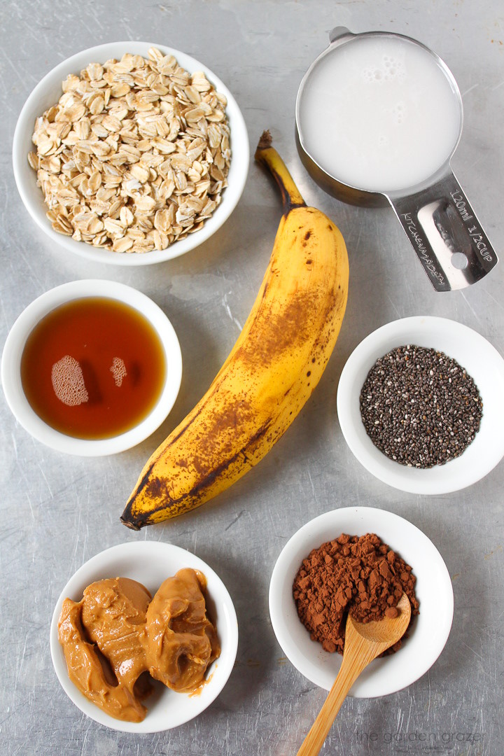 Overhead view of banana, dairy-free milk, cocoa powder, chia seeds, and peanut butter ingredients laid out on a metal tray