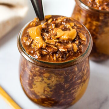Chunky monkey overnight oats served in small glass jars with a drizzle of peanut butter