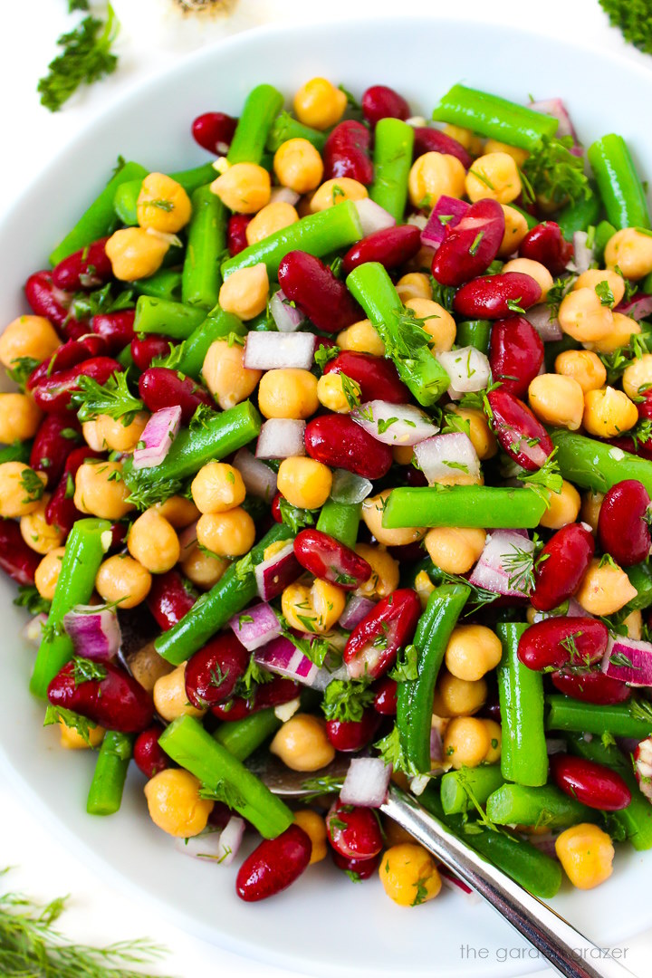 Overhead view of three bean salad in a white bowl with serving spoon