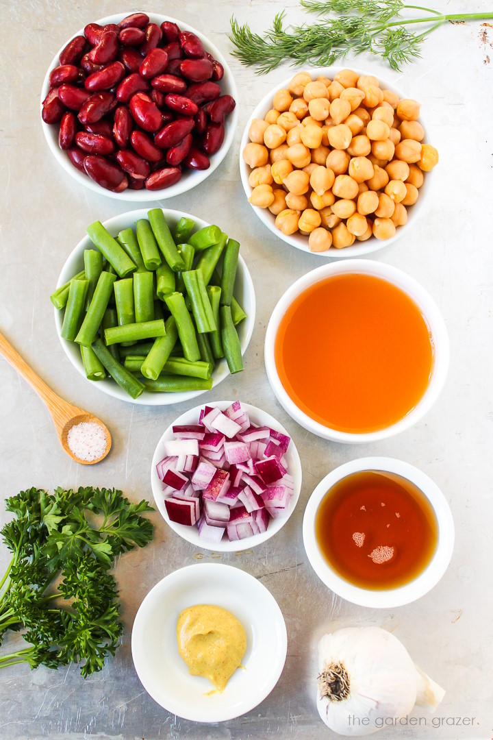 Kidney beans, chickpeas, green beans, vinegar, red onion, mustard, garlic, and fresh herb ingredients laid out on a metal tray