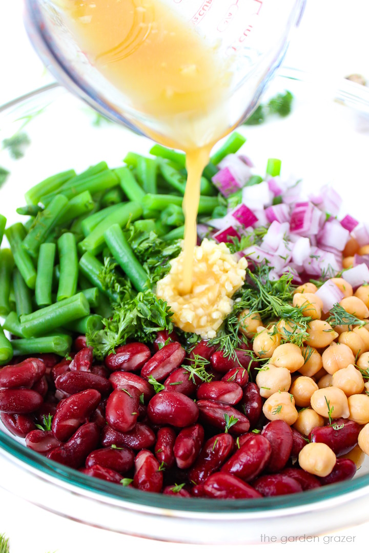 Vinegar dressing being poured over ingredients in a large glass bowl before mixing together