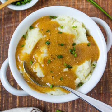 White bowl of mashed potatoes with easy vegan gravy on a wooden table
