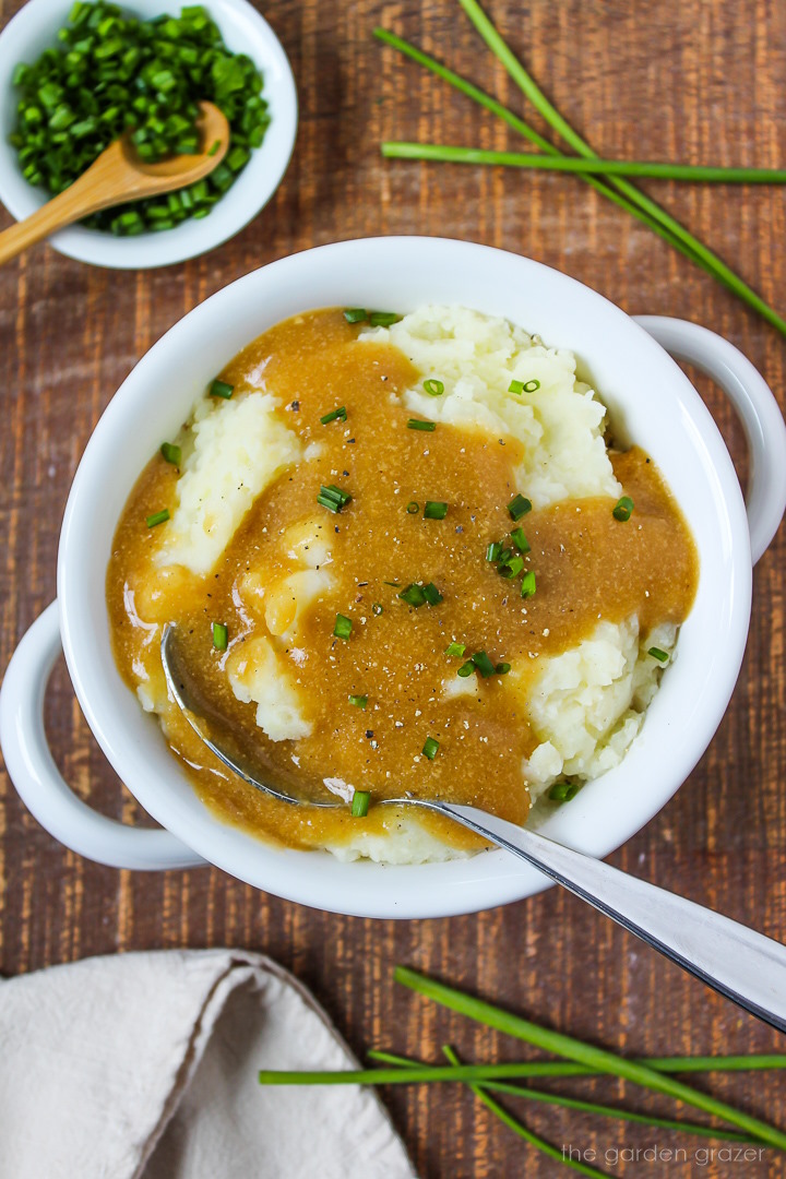 White bowl of mashed potatoes with easy vegan gravy on a wooden table