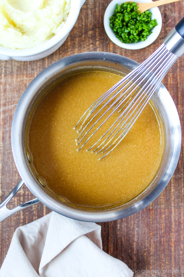 Overhead view of preparing vegan gravy in a small saucepan with a metal whisk