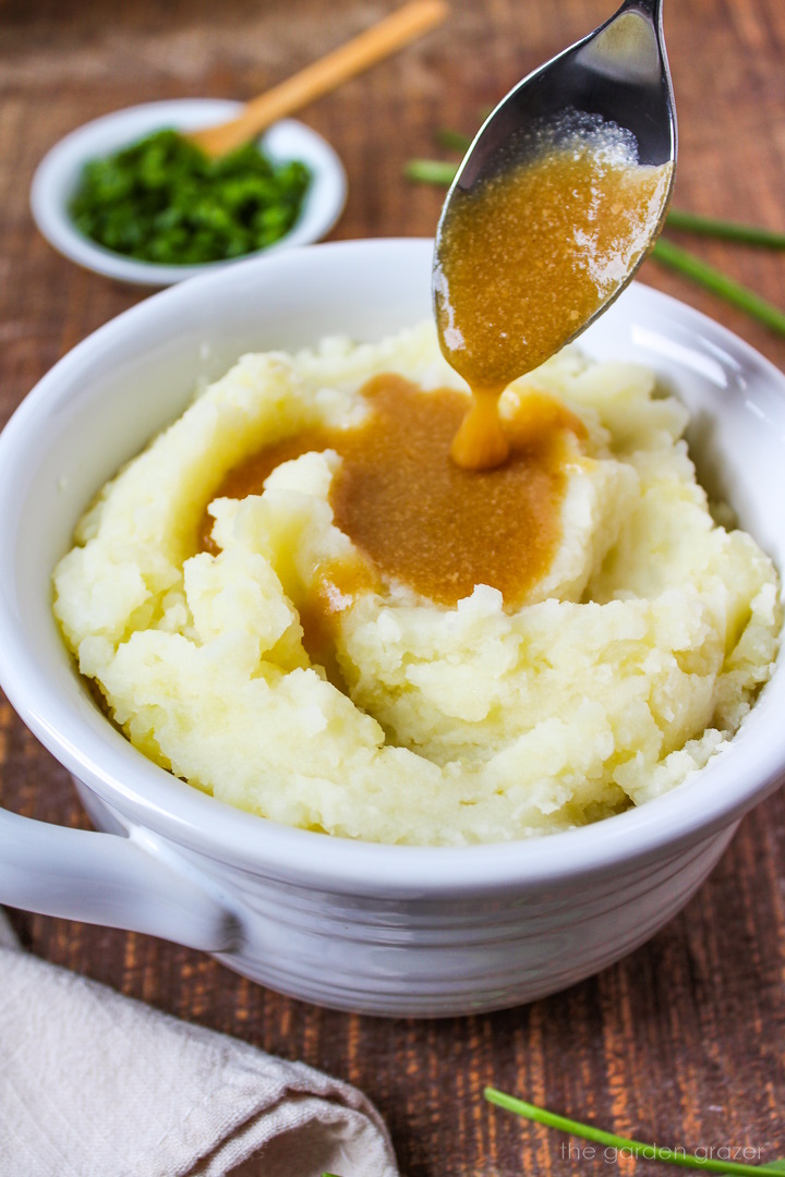 Serving spoon pouring gravy over a bowl of mashed potatoes