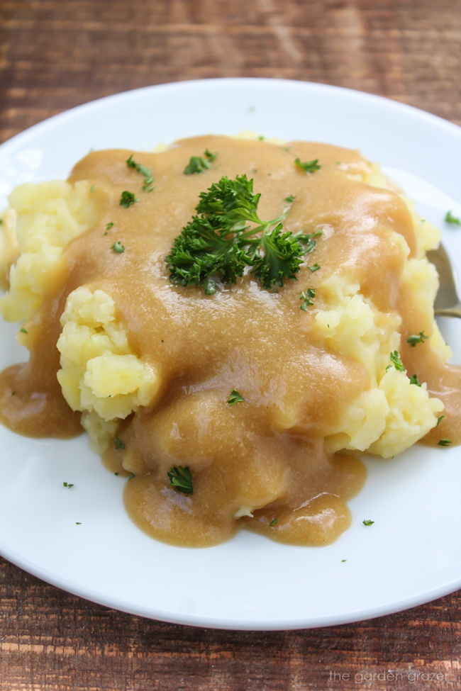 Vegan mashed potatoes and oil-free gravy on a white plate with fresh parsley