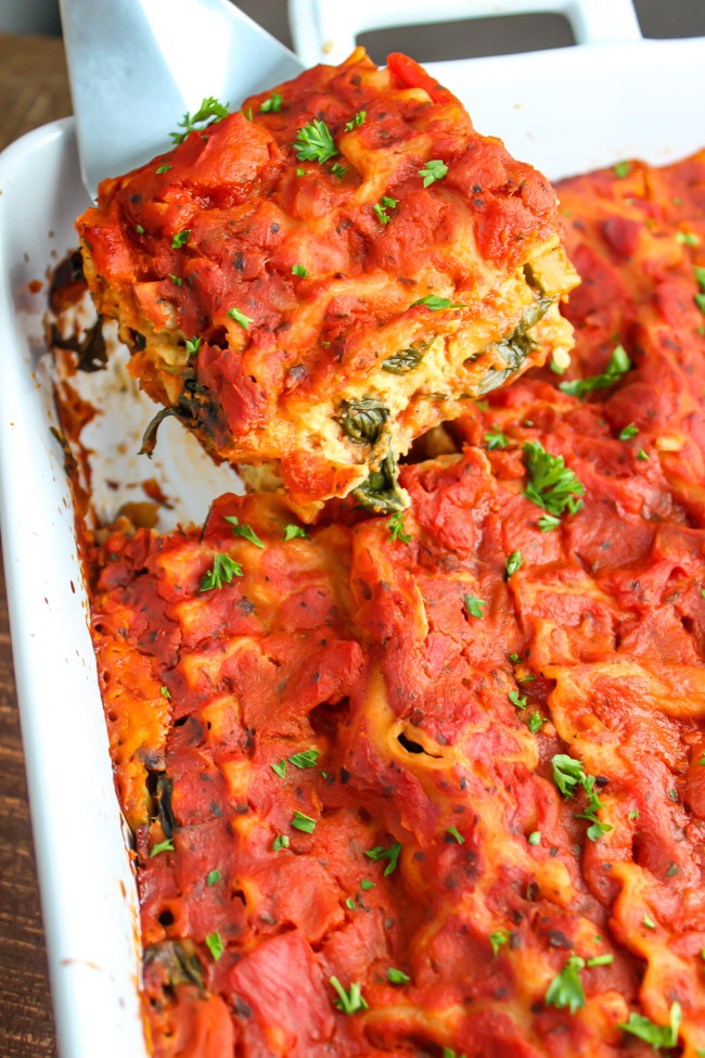 Metal spatula lifting out a piece of vegan lasagna from large baking dish