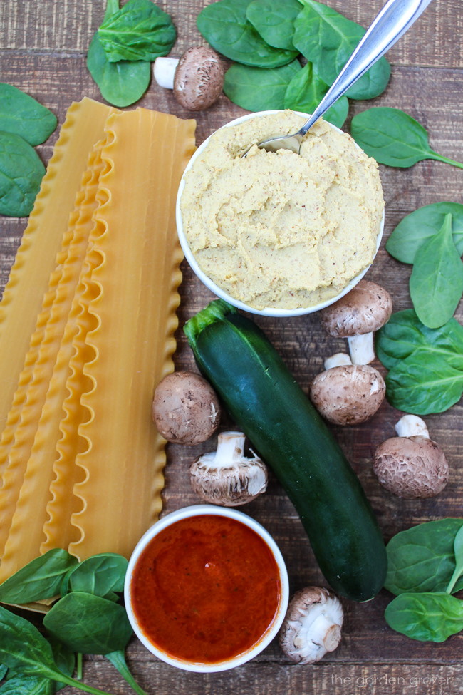 Noodles, dairy-free ricotta, tomato sauce, spinach, mushrooms, and zucchini ingredients on a wooden table