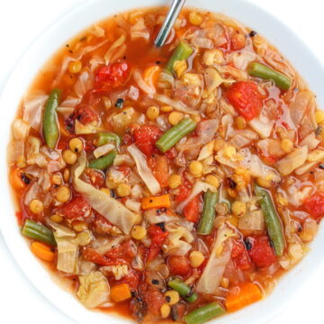 Vegan lentil and cabbage soup in a white bowl with spoon