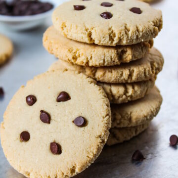 A stack of vegan almond maple cookies with chocolate chips on a sheet pan