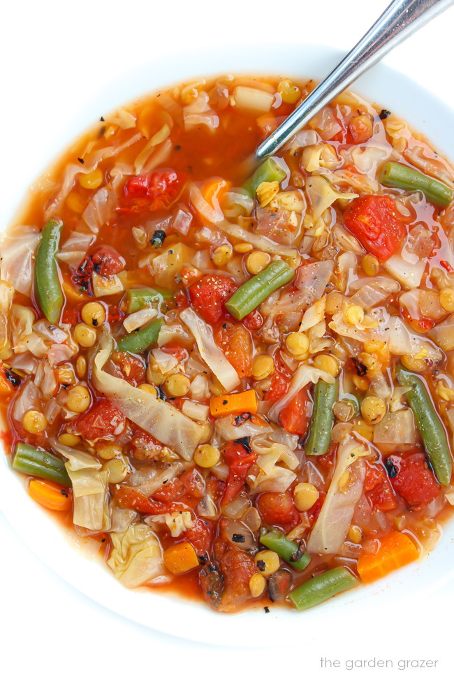White bowl of lentil cabbage soup with tomatoes and green beans