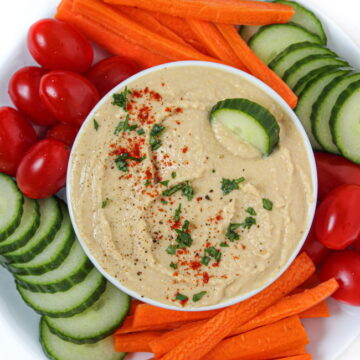 Oil-free hummus in a white bowl with sliced vegetables