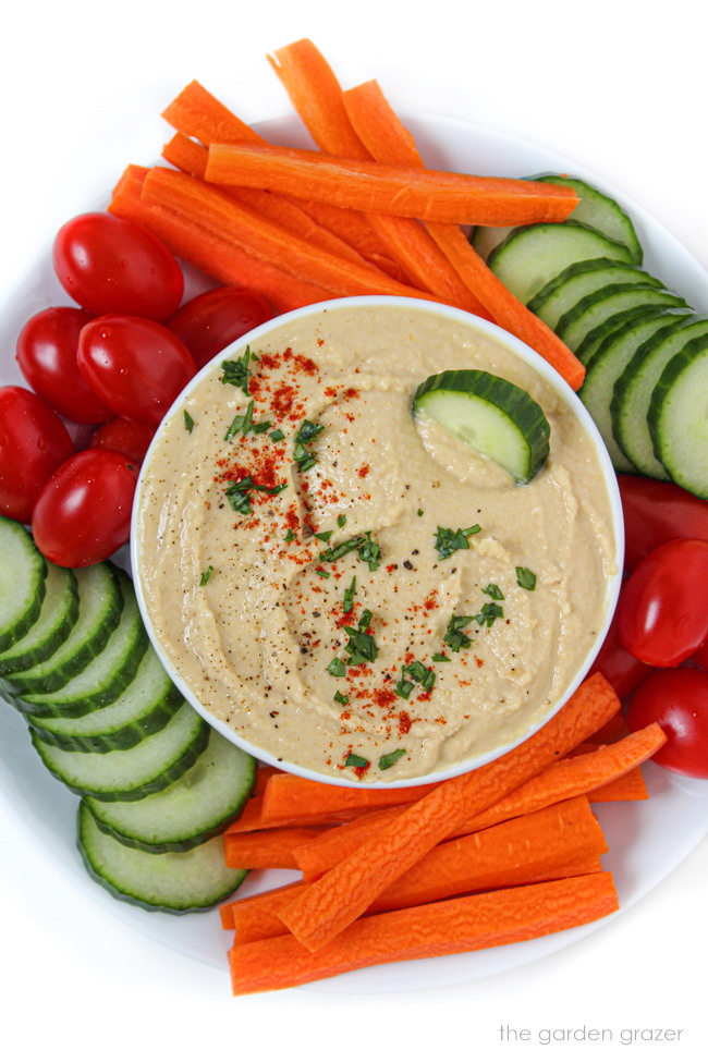 Oil-free hummus in a white bowl with sliced vegetables