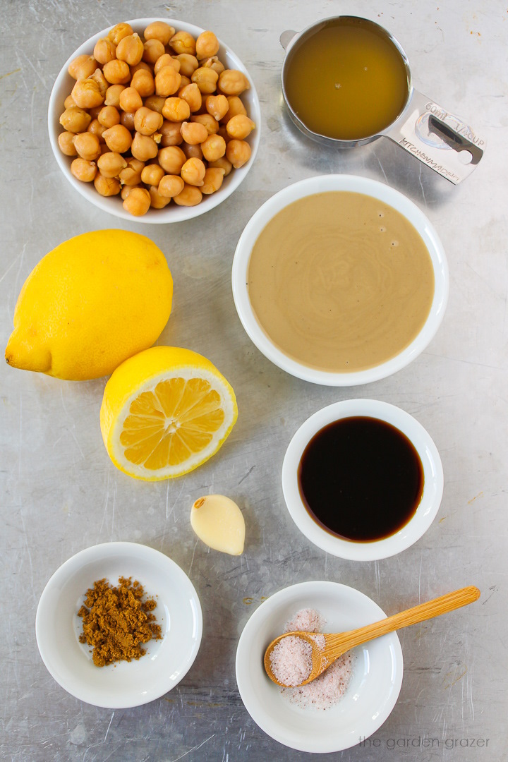 Chickpeas, tahini, lemons, ground cumin, garlic, and seasoning ingredients laid out on a metal tray