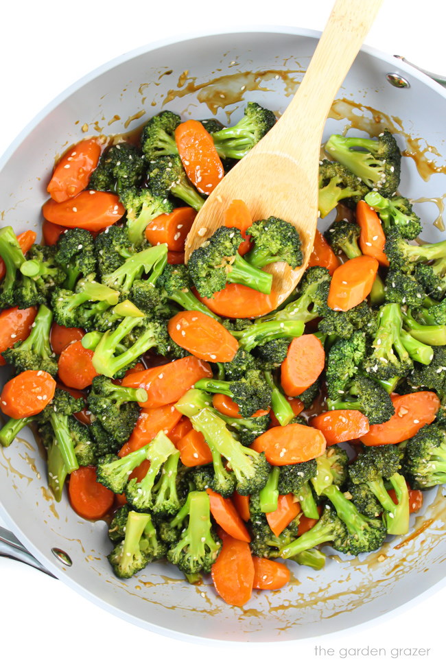 A skillet of fresh veggies cooking in sauce with wooden spoon