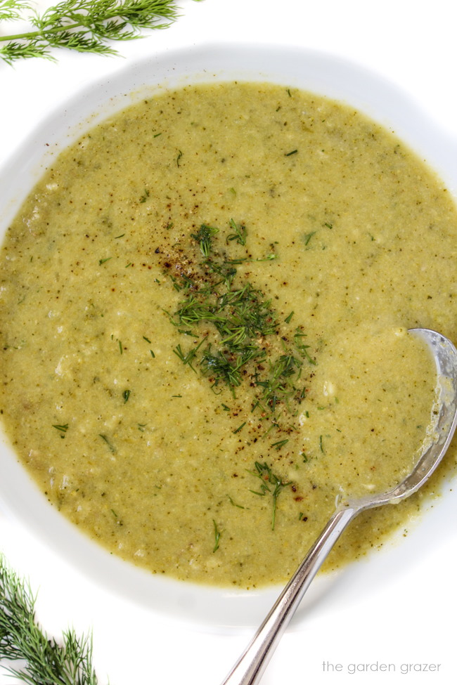 White bowl of vegan broccoli and potato soup with spoon and fresh dill