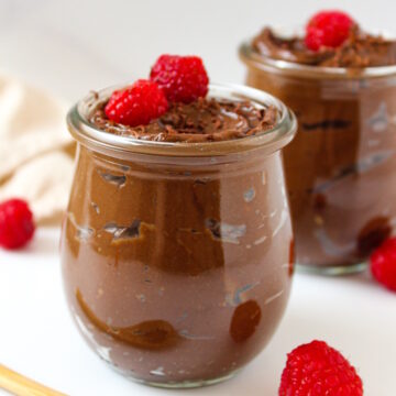 Avocado chocolate mousse served in small glass jars topped with fresh raspberries