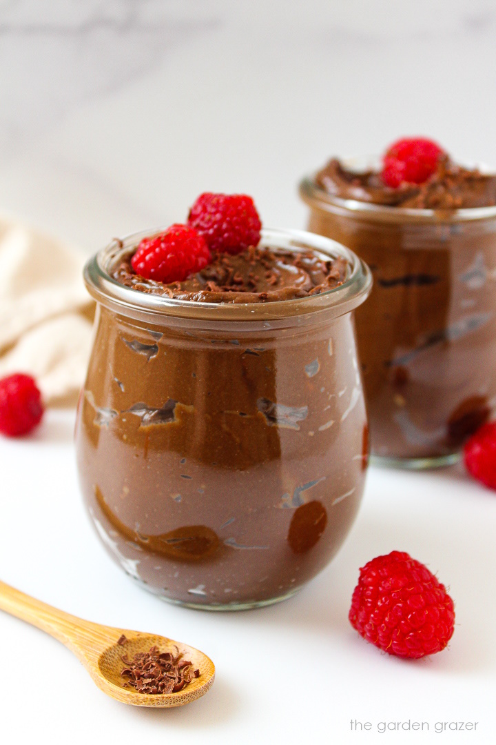 Avocado chocolate mousse served in small glass jars topped with fresh raspberries