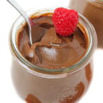 Vegan avocado chocolate mousse in a small glass jar with fresh raspberry on top